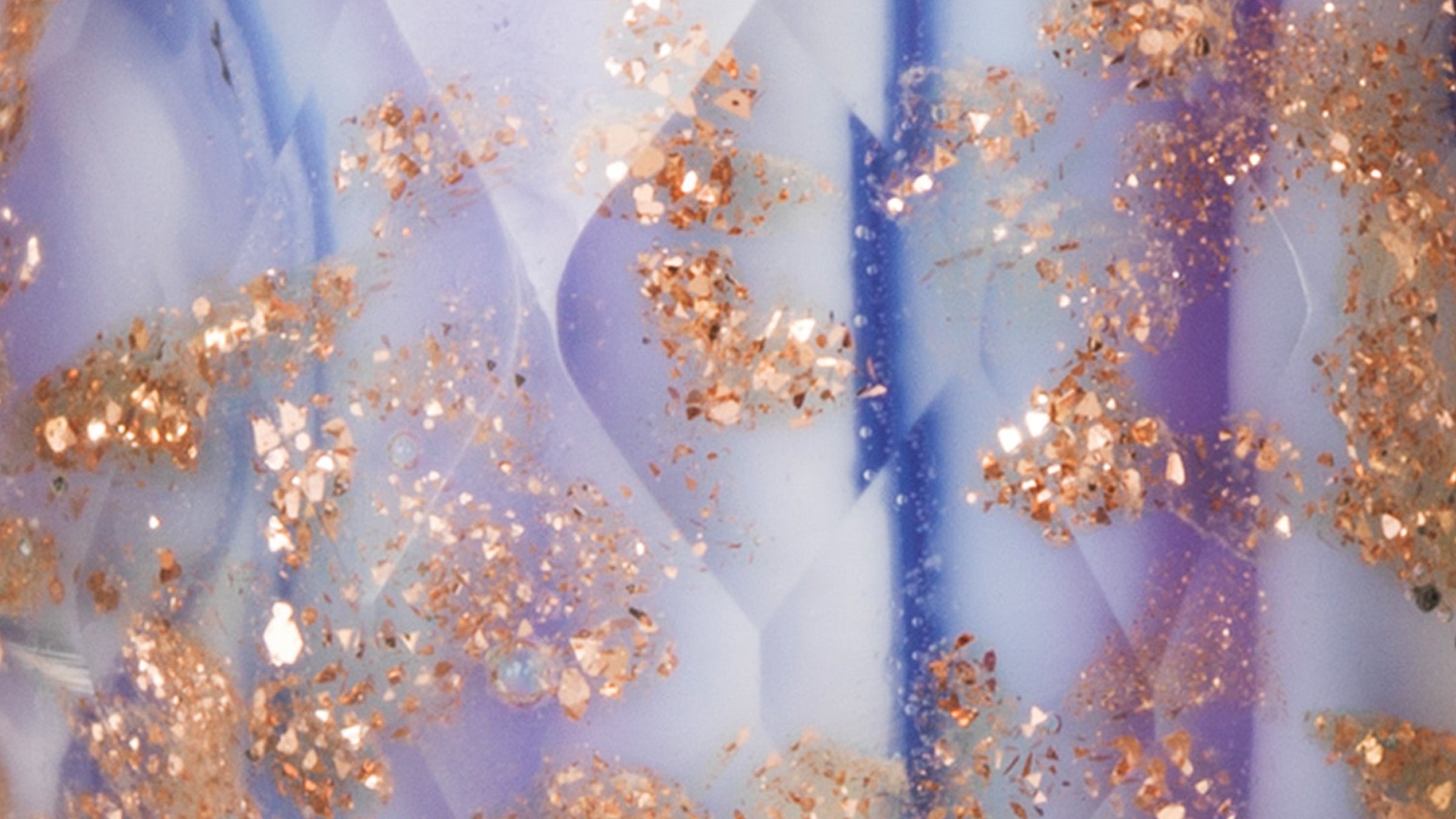 Gros plan sur la perle de verre Violet conviction. Cette perle de verre facetté présente des couleurs violettes et mauves dans un motif rayé, avec des paillettes dorées qui brillent à travers.