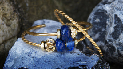 Jonc en Plaqué Or Trollbeads avec pierres bleues et perles dorées sur une roche 