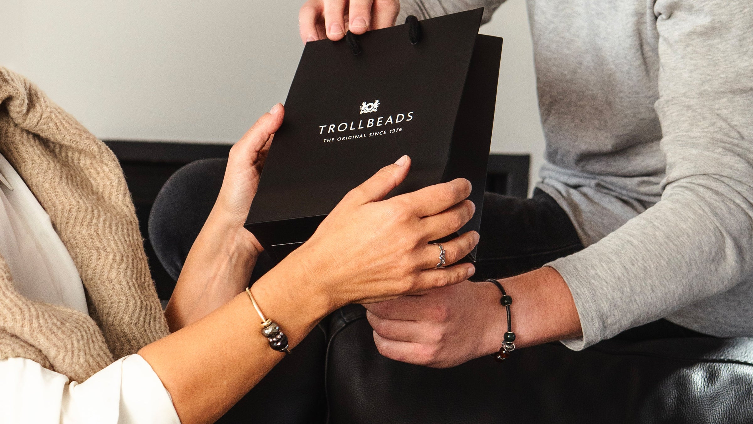 Two people holding a black TROLLBEADS branded gift bag.