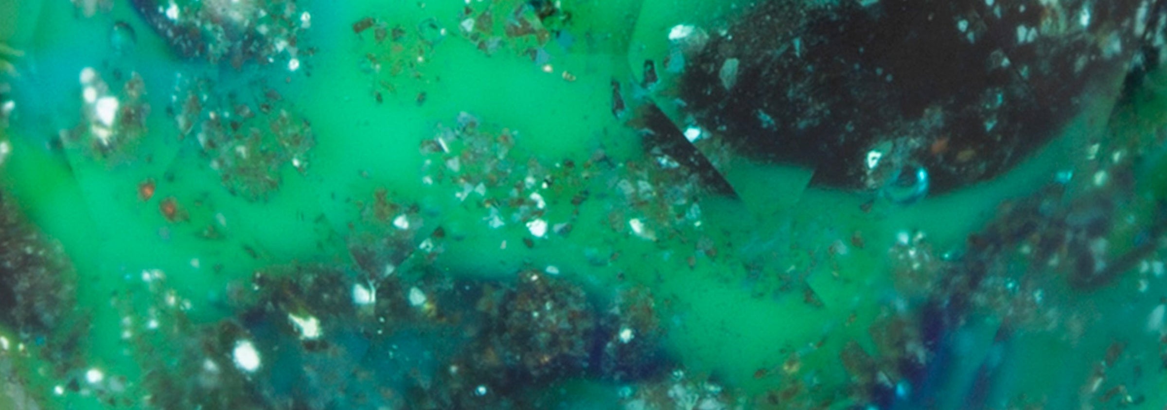 Gros plan sur une perle de verre de type émeraude. Des taches vertes et bleu foncé avec des paillettes composent cette perle de verre facettée et semblable à l'émeraude.